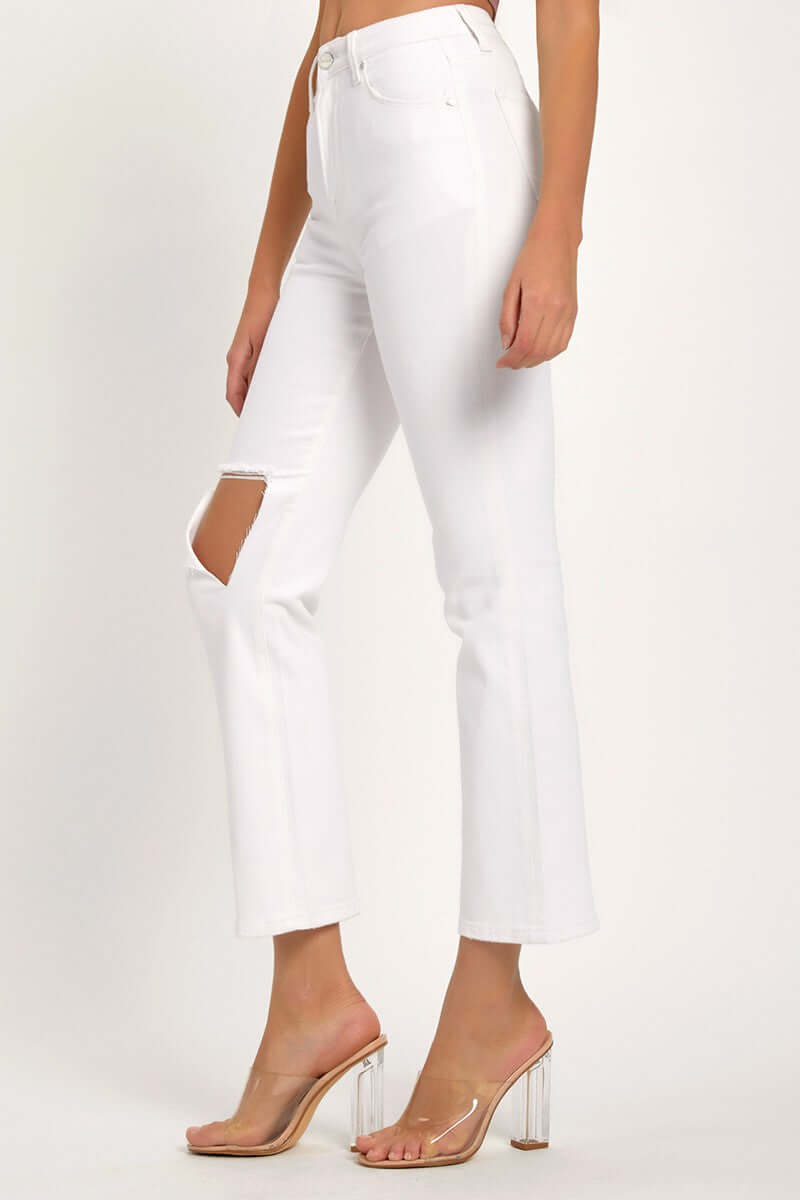 White distressed cropped straight jeans with knee rip and transparent heels, showcasing trendy and versatile denim fashion.