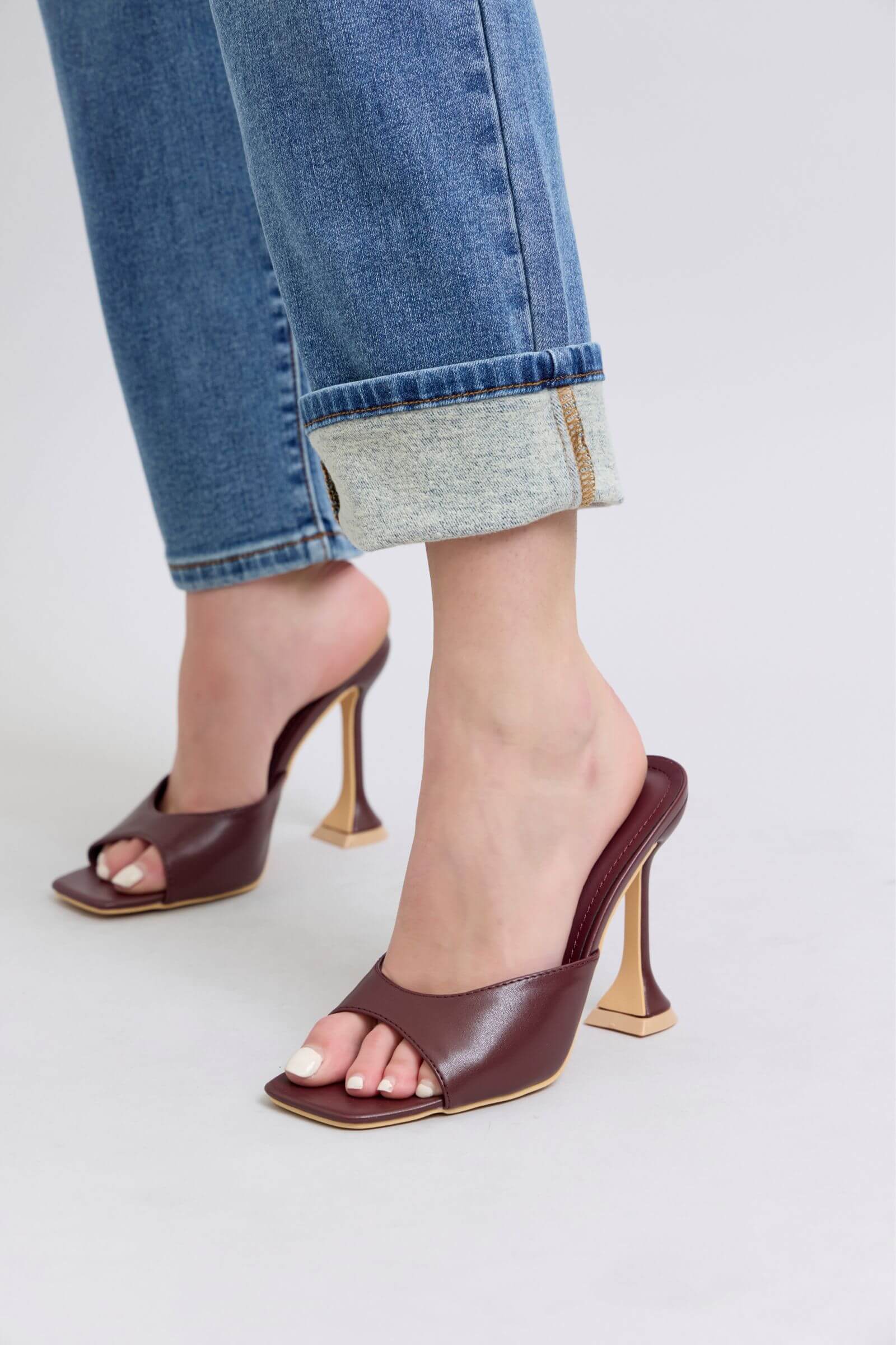 Stylish burgundy open-toe heels paired with rolled-up denim jeans for a chic, modern look.