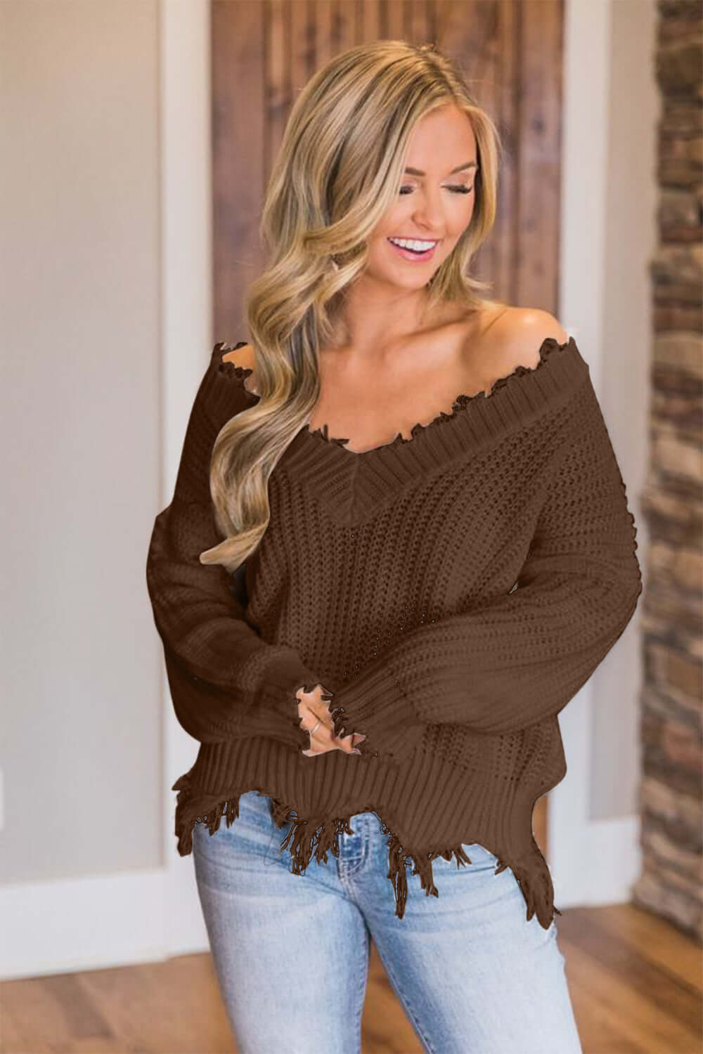 Woman wearing Bella Road frayed hem dropped shoulder sweater in brown, paired with jeans, showcasing casual and stylish fall fashion.