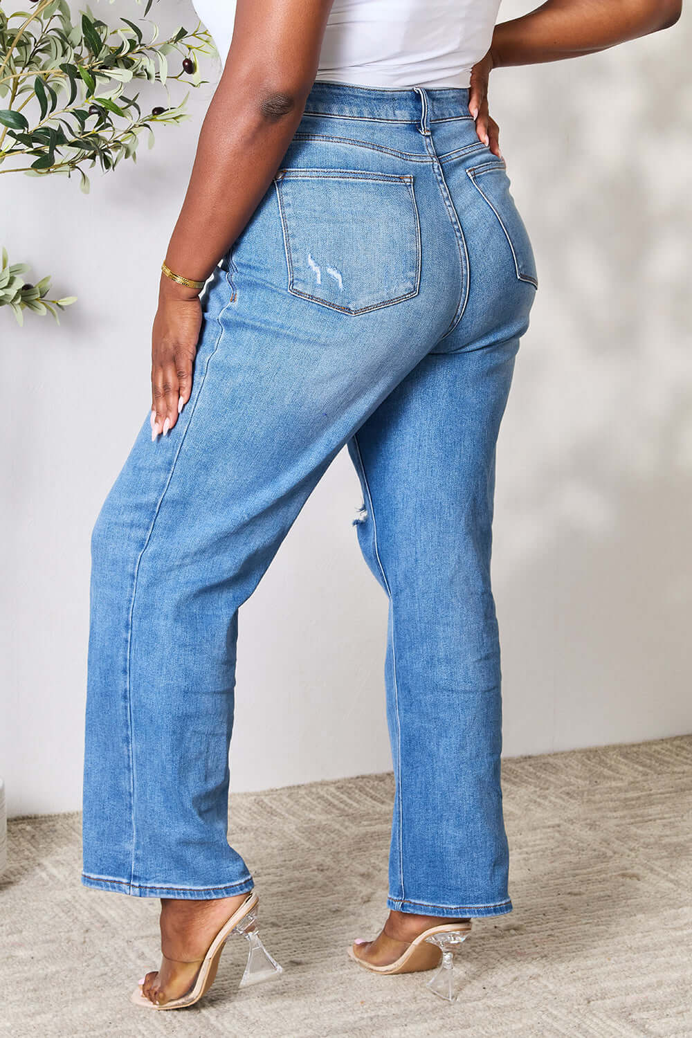 Woman wearing high waist distressed Judy Blue jeans in full size with back view to highlight the flattering fit and contemporary style.