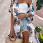 Woman in a stylish Bella Road Swim printed cover up with a Birds of Paradise pattern, paired with a white top and denim shorts.