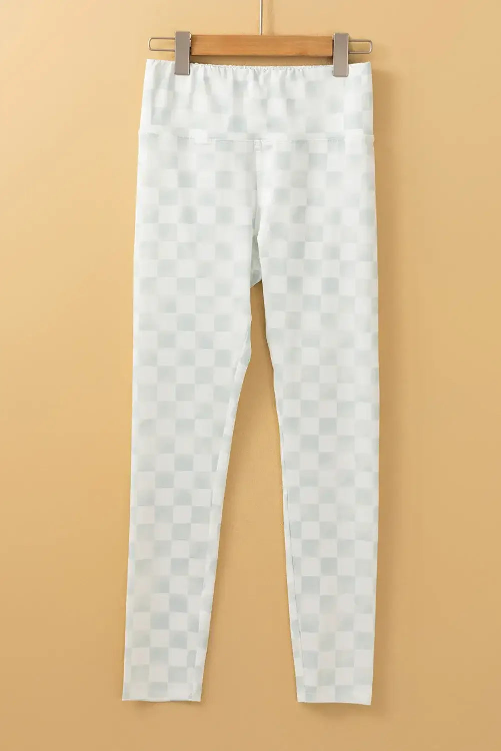 Bella Road white checkered elastic waist leggings hanging on a wooden hanger against a beige background