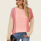 Stylish woman wearing a Double Take Texture Contrast Round Neck Long Sleeve T-Shirt in pink hues holding a black purse.