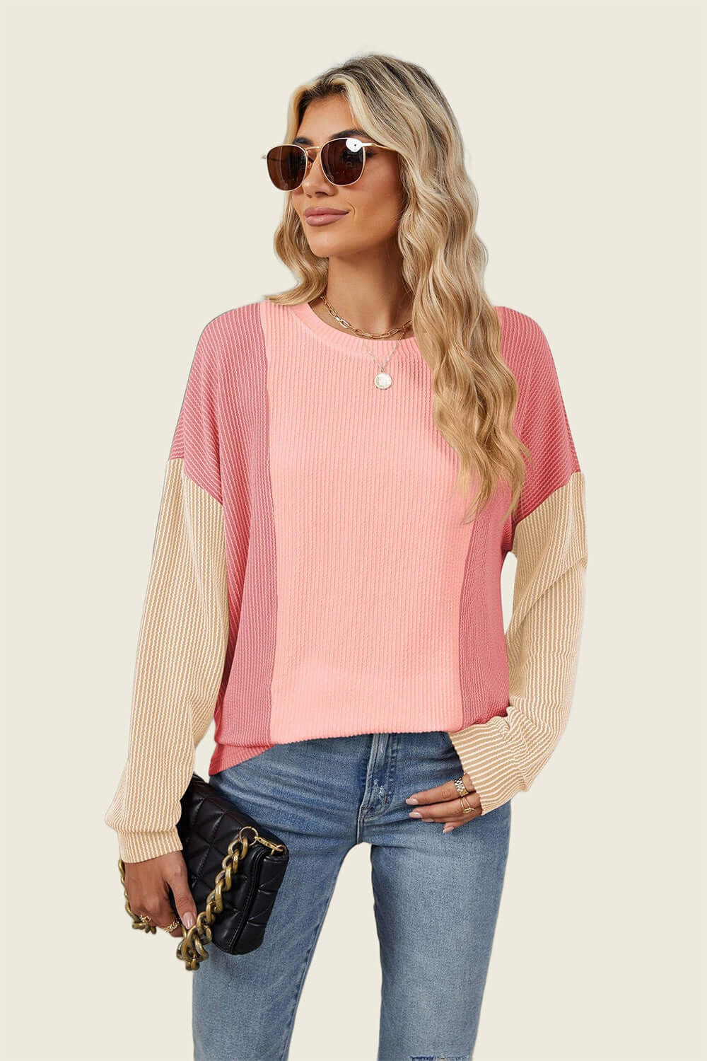 Stylish woman wearing a Double Take Texture Contrast Round Neck Long Sleeve T-Shirt in pink hues holding a black purse.