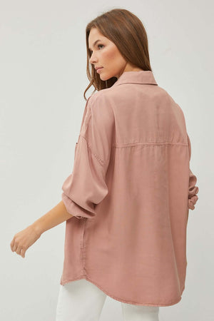 Back view of woman wearing a full-size, button-up, long-sleeve, pink denim shirt with white pants.