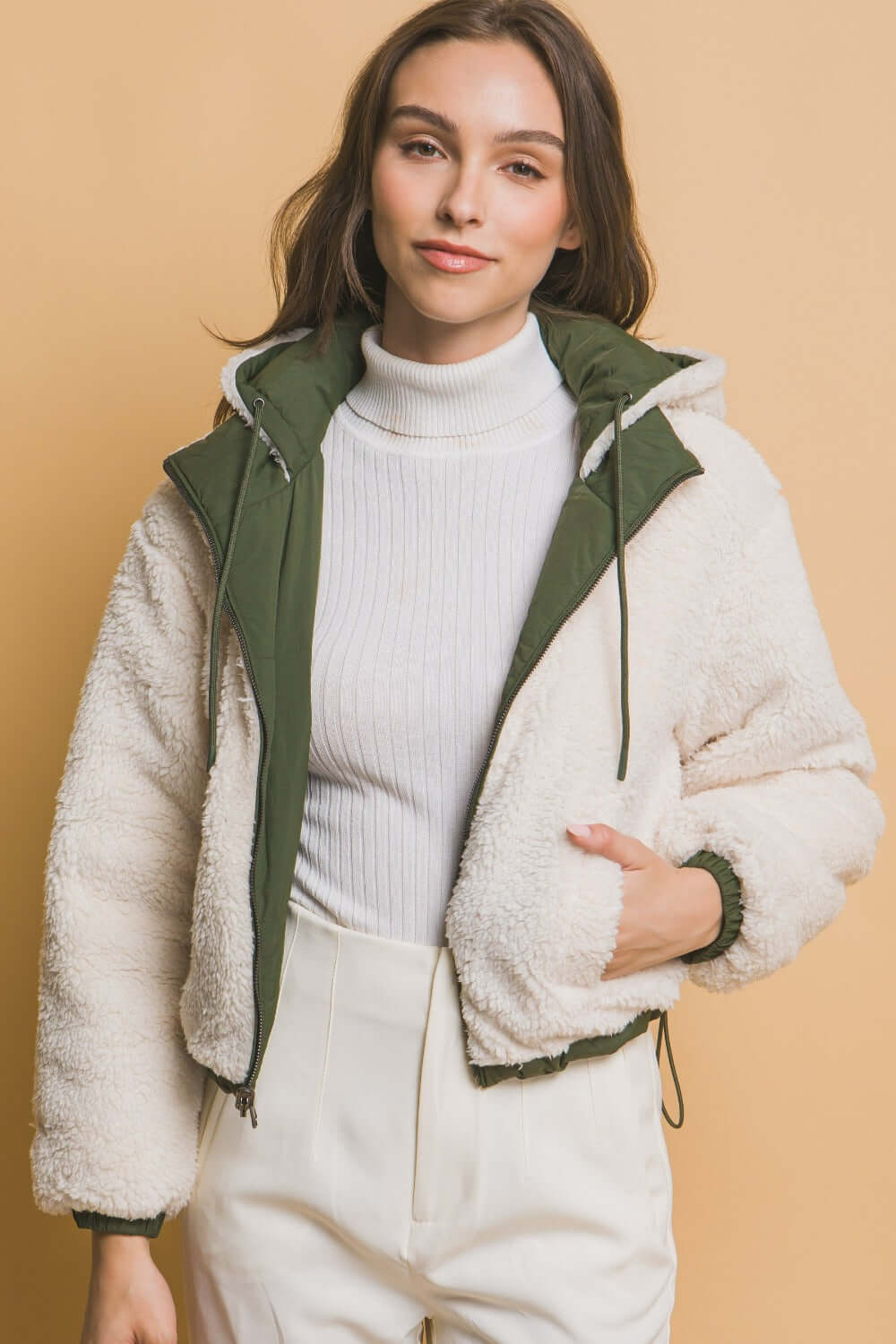 Woman wearing a Love Tree zip-up cropped hooded Sherpa reversible jacket in cream and green, showcasing its cozy and stylish design.