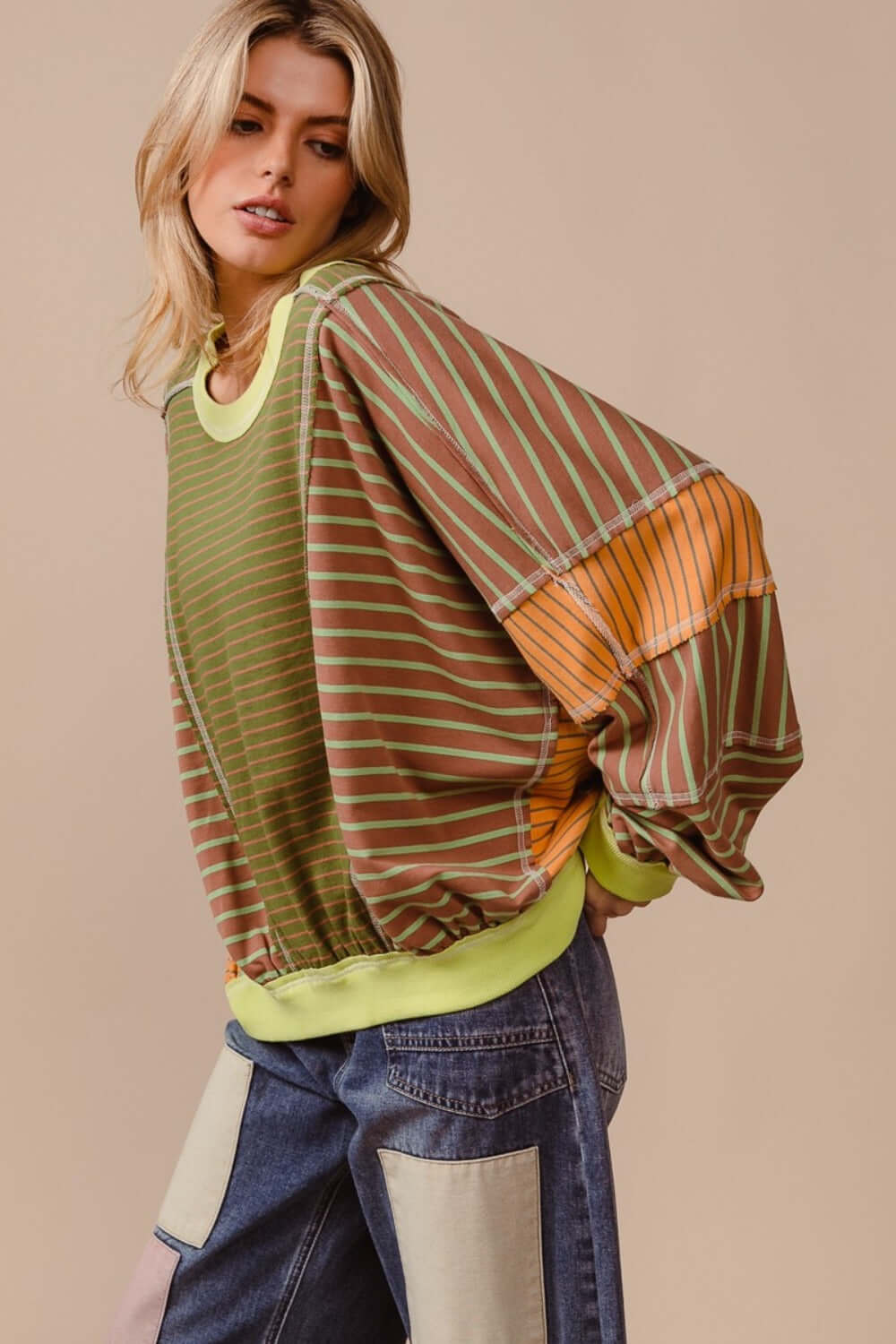 Woman wearing BiBi Color Block Striped Round Neck Sweatshirt with bold stripes in green, orange, and brown, styled with jeans.