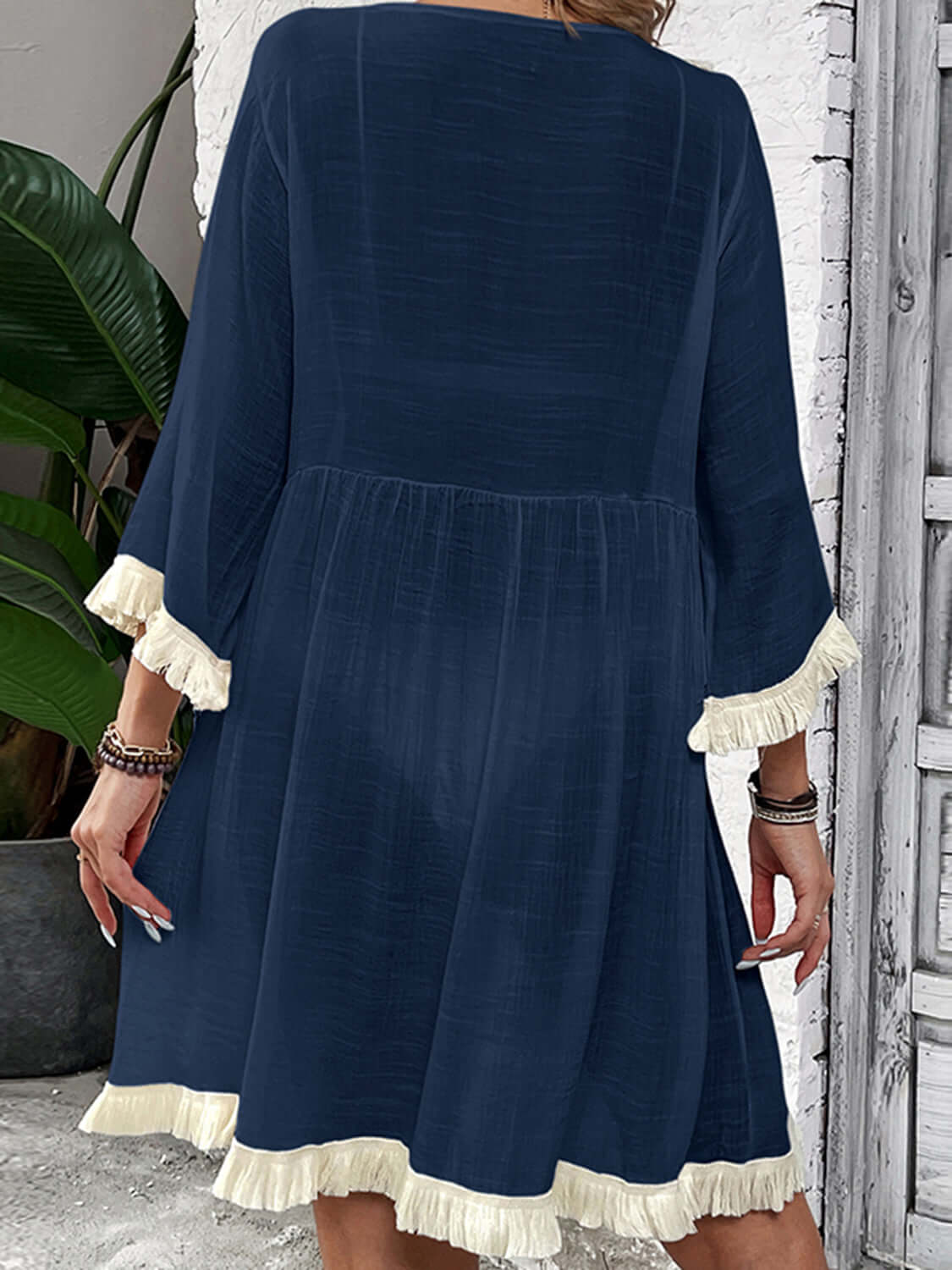 Woman wearing a navy blue Fringe Tie Neck Three-Quarter Sleeve Cover Up with white fringe accents on sleeves and hem.