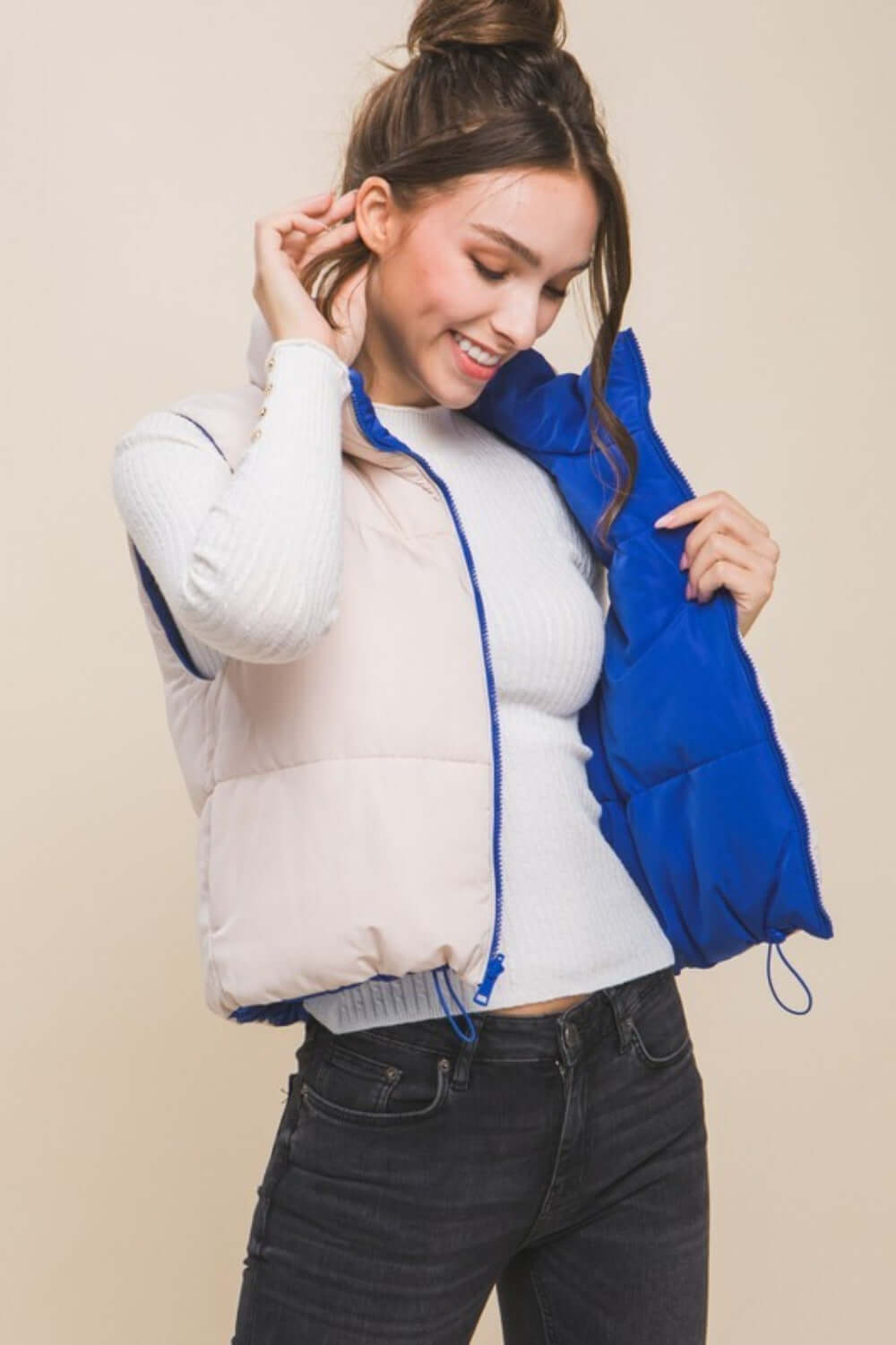 Model showcasing Love Tree zip-up cropped contrast reversible vest, smiling while holding the reversible side in blue.