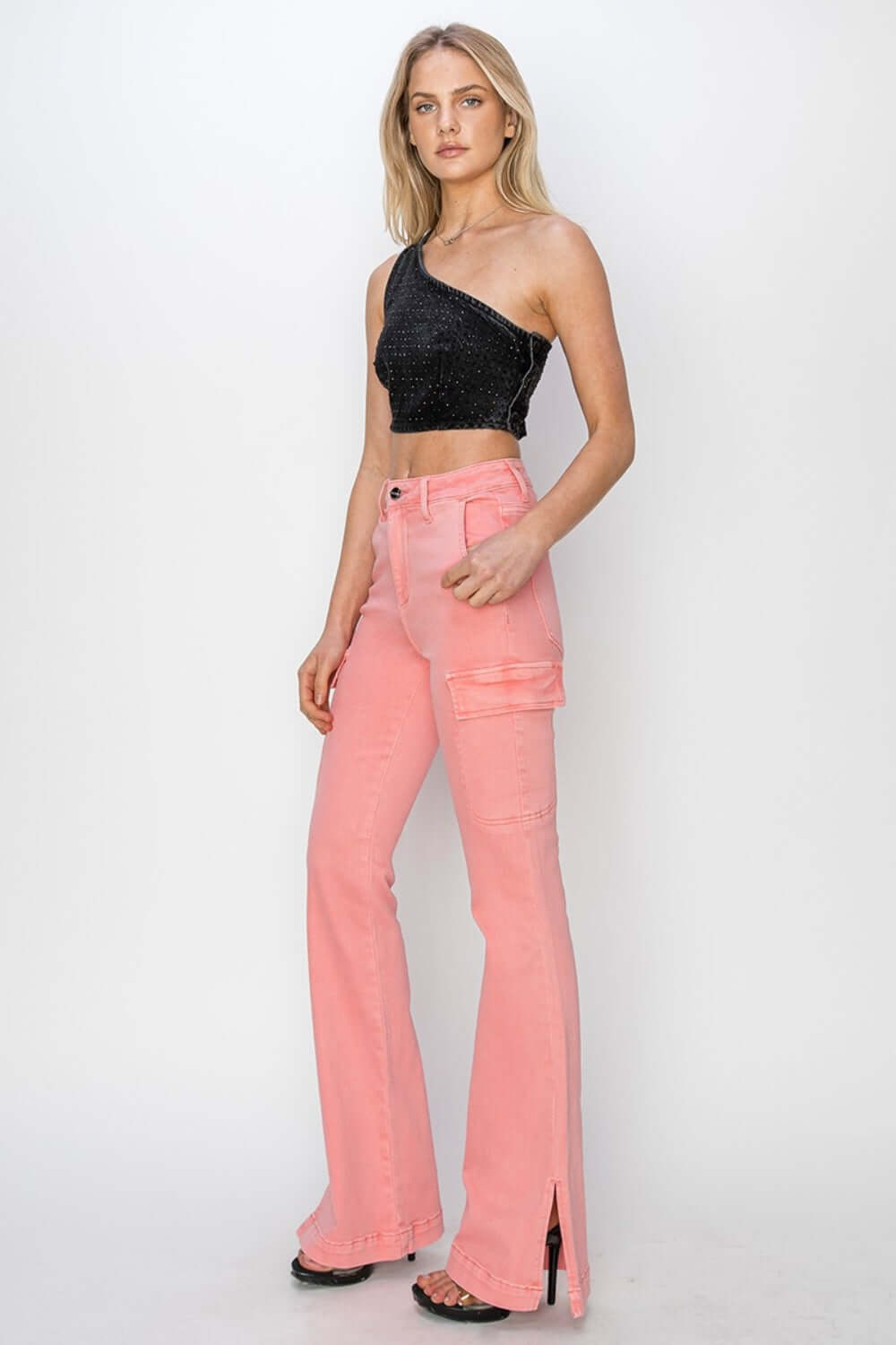 Model wearing high-rise side slit pink cargo bootcut jeans by Risen Jeans, styled with a black glittery one-shoulder top and heels