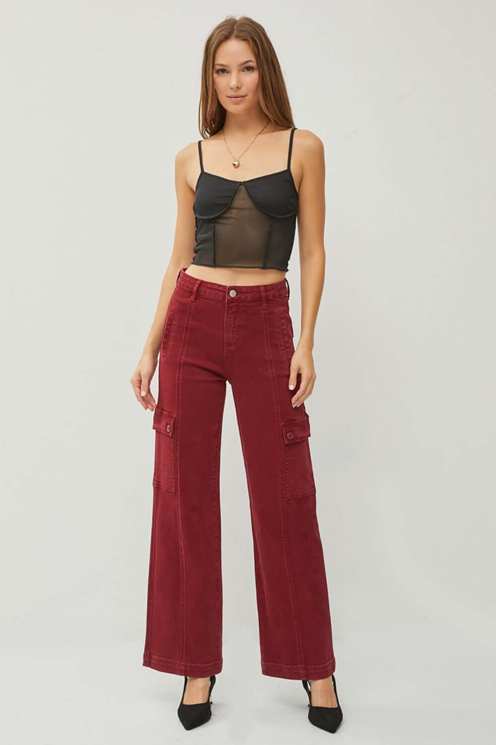 Woman wearing RISEN high rise wide leg cargo jeans in deep red, paired with a black top and heels. Trendy and stylish casual outfit.